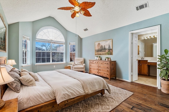 bedroom featuring vaulted ceiling, ensuite bath, a textured ceiling, and light hardwood / wood-style flooring