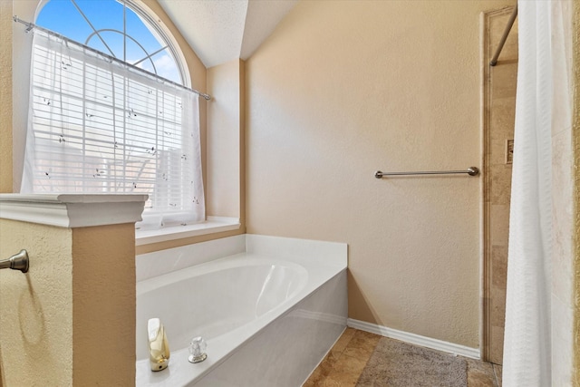 bathroom with lofted ceiling, a tub to relax in, tile patterned flooring, and a textured ceiling