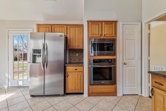 kitchen with light tile patterned flooring, stainless steel appliances, decorative backsplash, and dark stone counters