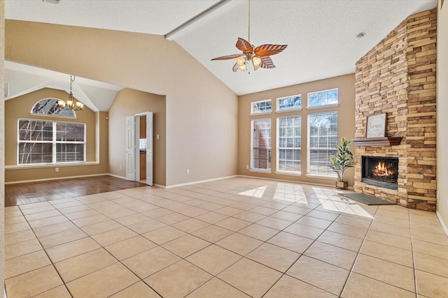 unfurnished living room with light tile patterned floors, ceiling fan with notable chandelier, high vaulted ceiling, a stone fireplace, and beamed ceiling