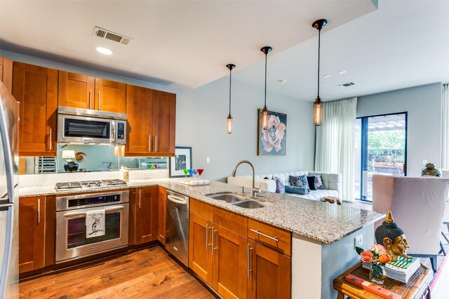 kitchen with sink, light stone counters, hanging light fixtures, kitchen peninsula, and stainless steel appliances