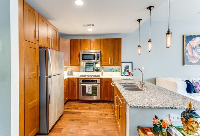 kitchen featuring sink, hanging light fixtures, stainless steel appliances, light stone countertops, and kitchen peninsula