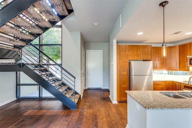 kitchen featuring sink, hanging light fixtures, stainless steel appliances, dark hardwood / wood-style floors, and light stone counters