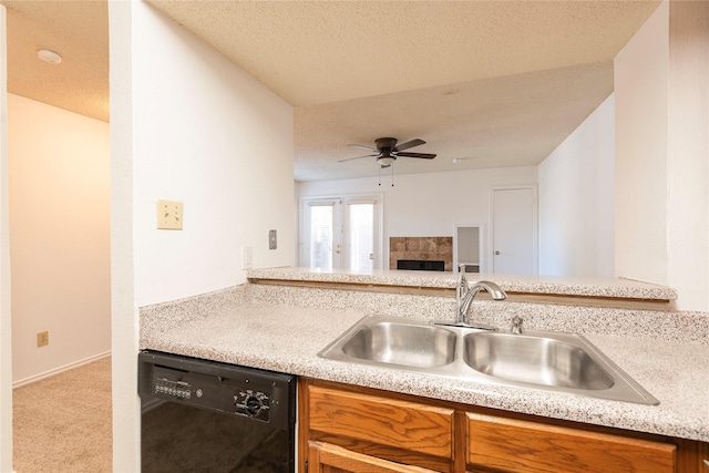 kitchen with sink, dishwasher, a fireplace, a textured ceiling, and light colored carpet