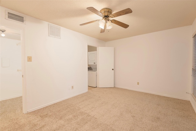 unfurnished room featuring light carpet, ceiling fan, and stacked washer / dryer