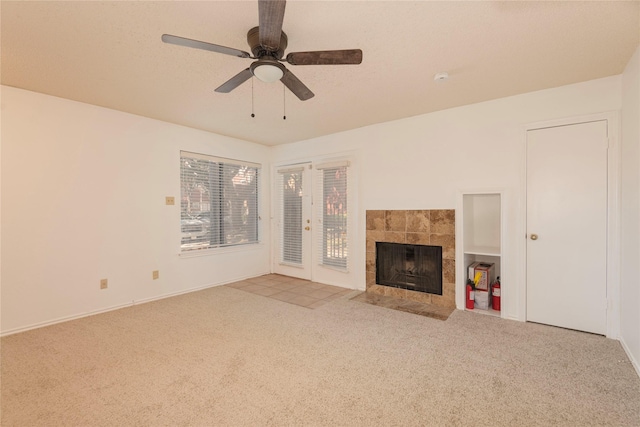 unfurnished living room with ceiling fan, light colored carpet, a tiled fireplace, and a textured ceiling