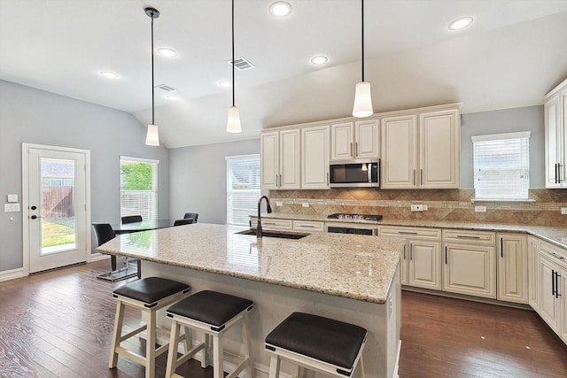 kitchen with hanging light fixtures, an island with sink, sink, and light stone counters