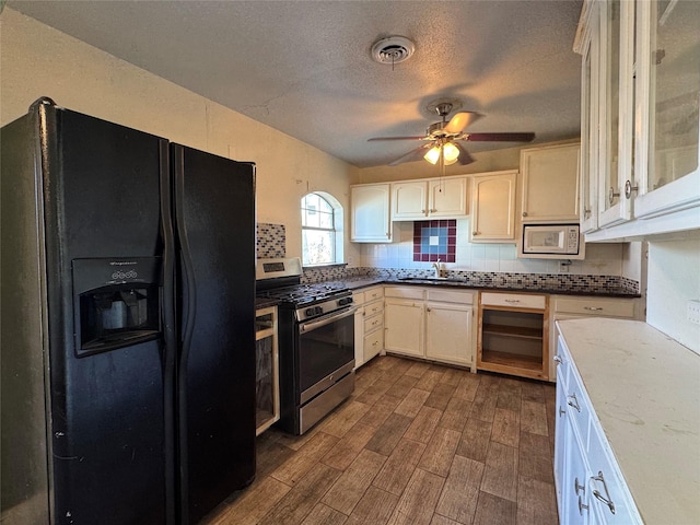 kitchen featuring white microwave, sink, decorative backsplash, black fridge with ice dispenser, and stainless steel range with gas stovetop