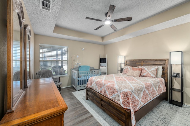 bedroom with hardwood / wood-style flooring, ceiling fan, a textured ceiling, and a tray ceiling