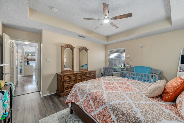 bedroom featuring ceiling fan, dark hardwood / wood-style floors, a textured ceiling, and a tray ceiling