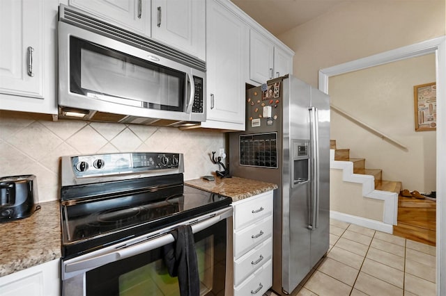 kitchen featuring white cabinetry, light stone counters, light tile patterned floors, stainless steel appliances, and backsplash