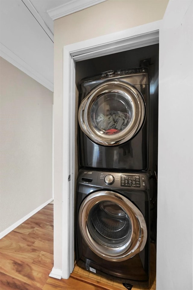 laundry area featuring stacked washer and dryer, ornamental molding, and hardwood / wood-style floors