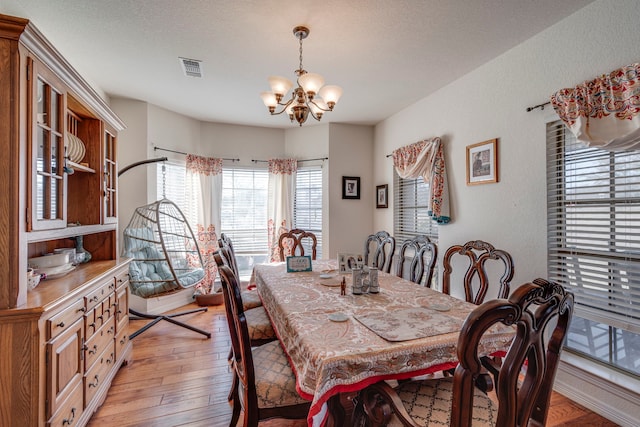 dining room featuring a textured ceiling, an inviting chandelier, and light hardwood / wood-style flooring