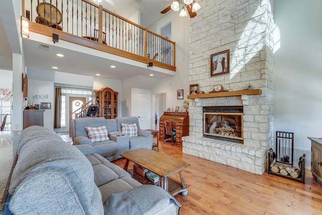 living room with a stone fireplace, a towering ceiling, ceiling fan, and light wood-type flooring