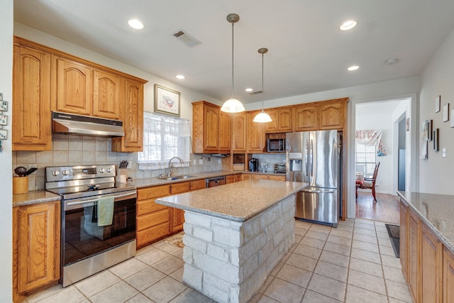 kitchen featuring sink, hanging light fixtures, a center island, stainless steel appliances, and light stone countertops