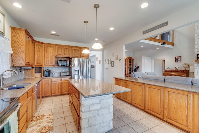 kitchen with sink, light stone counters, decorative light fixtures, appliances with stainless steel finishes, and a kitchen island