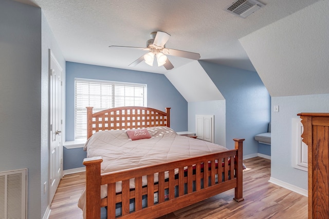 bedroom with lofted ceiling, a textured ceiling, and light wood-type flooring