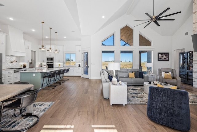 living room with sink, high vaulted ceiling, ceiling fan, and light wood-type flooring