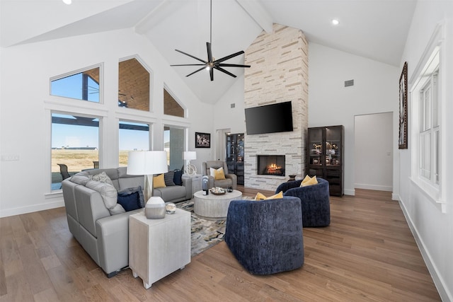 living room featuring a stone fireplace, high vaulted ceiling, beamed ceiling, ceiling fan, and hardwood / wood-style floors