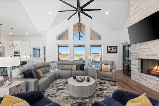 living room with wood-type flooring, high vaulted ceiling, ceiling fan, and a fireplace