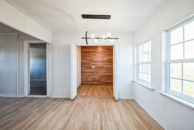 unfurnished dining area with an inviting chandelier, crown molding, light hardwood / wood-style flooring, and wood walls