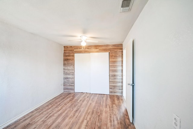 unfurnished bedroom featuring wood-type flooring, a closet, ceiling fan, and wood walls