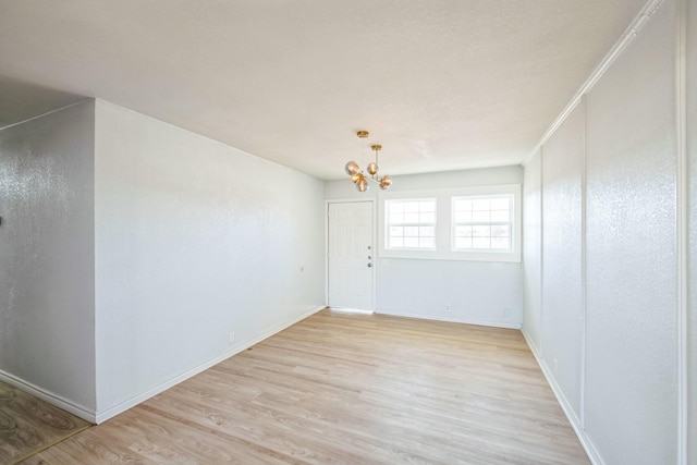 spare room with a notable chandelier and light hardwood / wood-style flooring