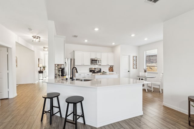 kitchen with sink, white cabinetry, light wood-type flooring, appliances with stainless steel finishes, and kitchen peninsula