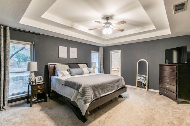 bedroom featuring light carpet, connected bathroom, and a tray ceiling