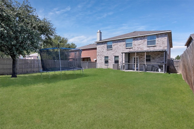 rear view of property with a yard and a trampoline