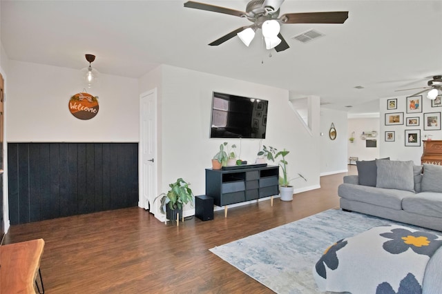 living room featuring dark wood-type flooring, ceiling fan, and wooden walls