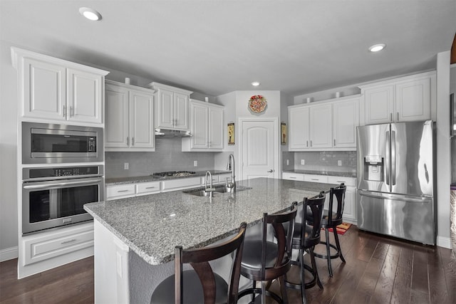 kitchen featuring white cabinetry, dark hardwood / wood-style flooring, a kitchen island with sink, stainless steel appliances, and light stone countertops