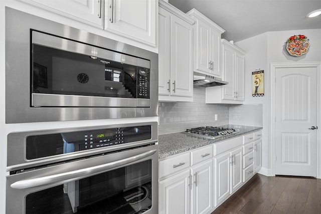 kitchen with appliances with stainless steel finishes, white cabinetry, backsplash, dark hardwood / wood-style flooring, and light stone counters