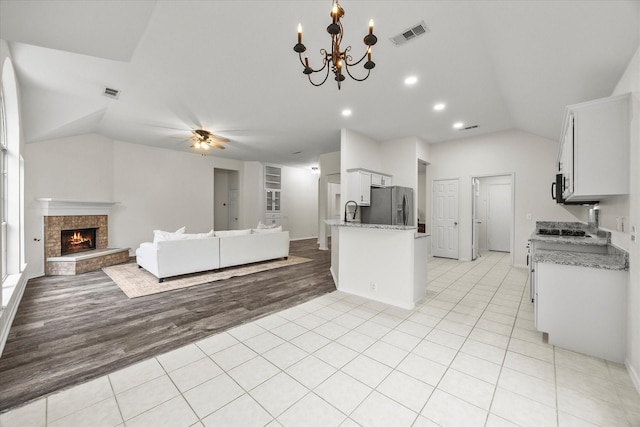 kitchen with lofted ceiling, white cabinetry, stainless steel refrigerator with ice dispenser, light stone counters, and light tile patterned flooring