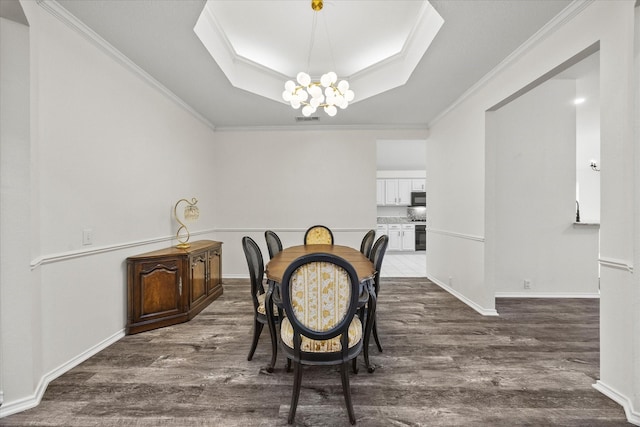 dining room featuring dark wood-type flooring, a tray ceiling, crown molding, and a notable chandelier