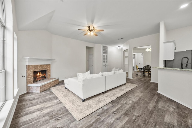 living room with a tile fireplace, vaulted ceiling, ceiling fan, and dark hardwood / wood-style flooring