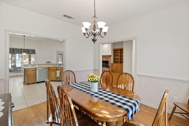 dining area featuring sink, a chandelier, built in features, a fireplace, and light hardwood / wood-style floors