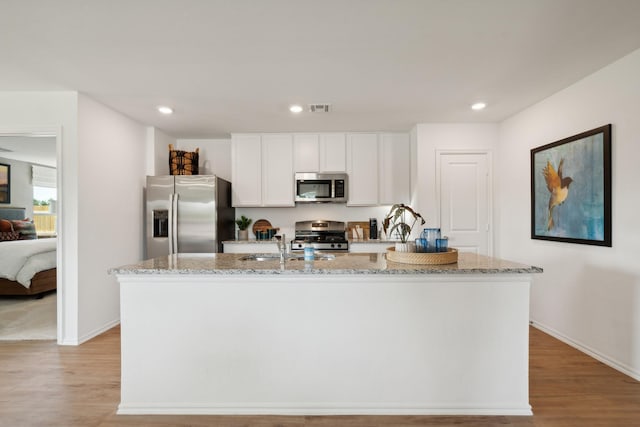 kitchen with light stone counters, stainless steel appliances, an island with sink, and white cabinets