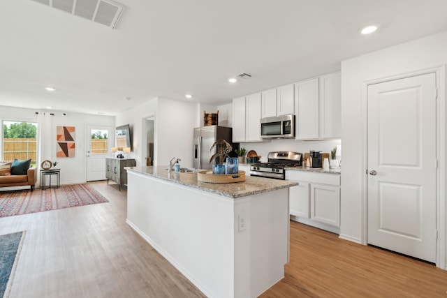 kitchen featuring appliances with stainless steel finishes, a kitchen island with sink, white cabinets, and light hardwood / wood-style floors