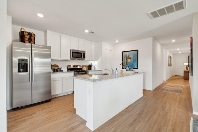 kitchen featuring sink, appliances with stainless steel finishes, white cabinetry, light hardwood / wood-style floors, and a center island with sink