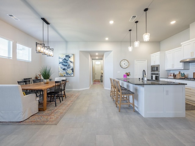 kitchen with hanging light fixtures, white cabinets, dark stone counters, and a spacious island