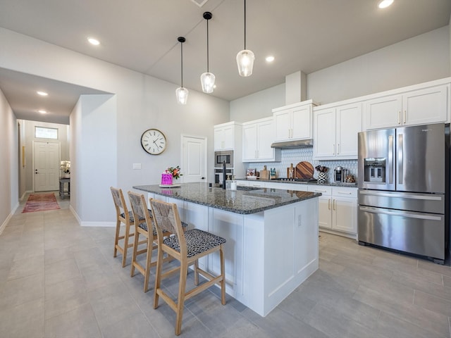 kitchen with appliances with stainless steel finishes, white cabinetry, an island with sink, decorative backsplash, and dark stone counters