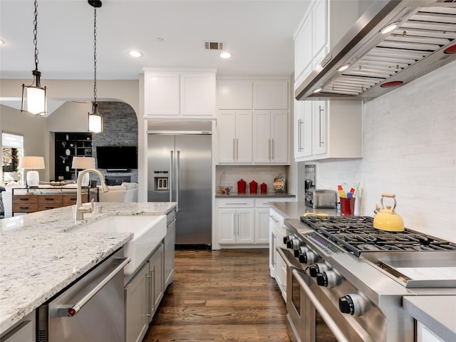 kitchen featuring wall chimney exhaust hood, white cabinetry, light stone counters, hanging light fixtures, and premium appliances