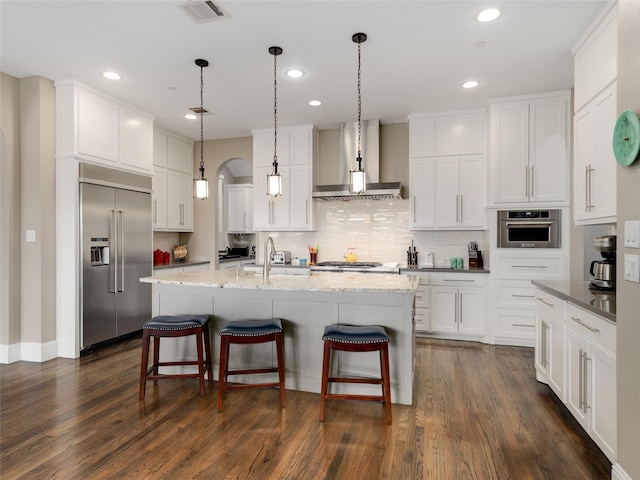 kitchen featuring appliances with stainless steel finishes, white cabinetry, sink, a kitchen island with sink, and wall chimney range hood