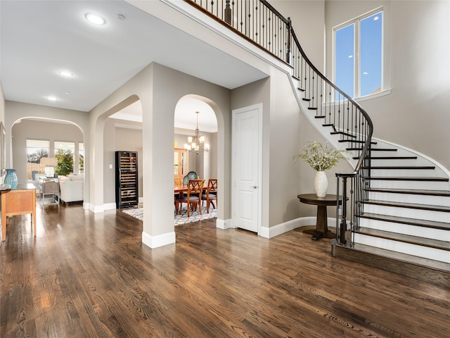 entrance foyer with a towering ceiling, a chandelier, beverage cooler, and dark hardwood / wood-style flooring