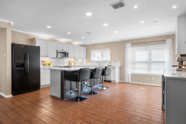 kitchen with a kitchen bar, a center island, white cabinets, and appliances with stainless steel finishes