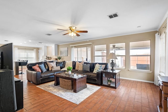 living room with a wealth of natural light, wood-type flooring, ornamental molding, and ceiling fan