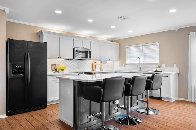 kitchen featuring black fridge with ice dispenser, sink, white cabinetry, a kitchen breakfast bar, and a kitchen island