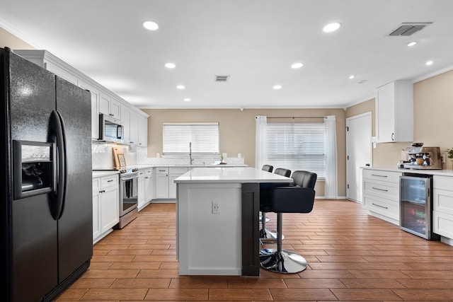 kitchen with a breakfast bar area, white cabinetry, stainless steel appliances, a center island, and beverage cooler