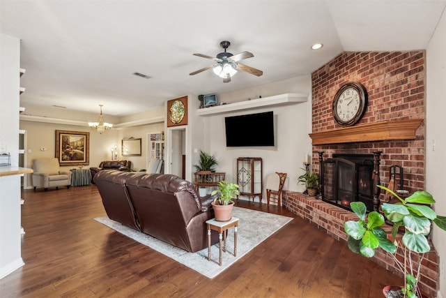 living room featuring lofted ceiling, dark wood-type flooring, a fireplace, and ceiling fan with notable chandelier